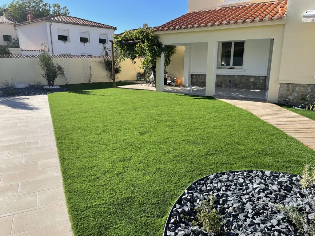 Pelouse artificielle : aménagement moderne du jardin et terrasse bois Aménagement extérieur de maison: gazon synthétique lumineux, allée en dalles beiges et chemin en bois menant à la terrasse couverte.