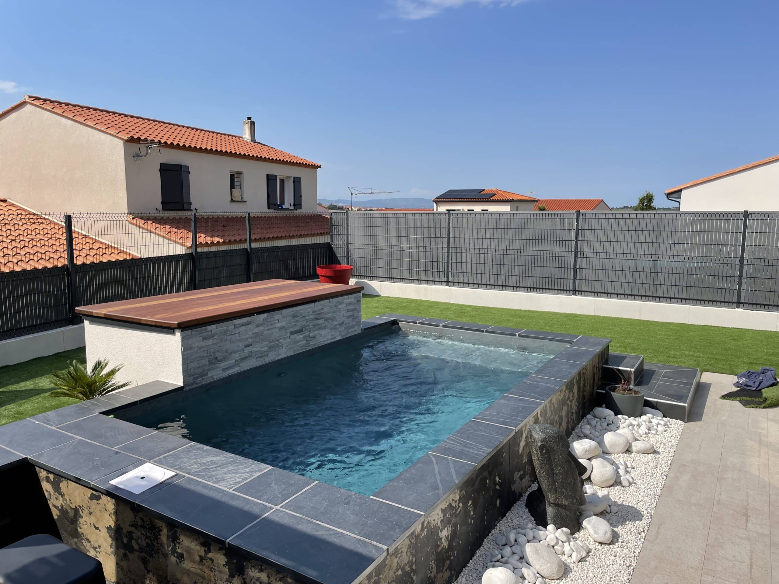 Mini-piscine contemporaine avec margelles en ardoise et couverture bois. Jardin avec gazon et clôture privée dans un cadre résidentiel.
