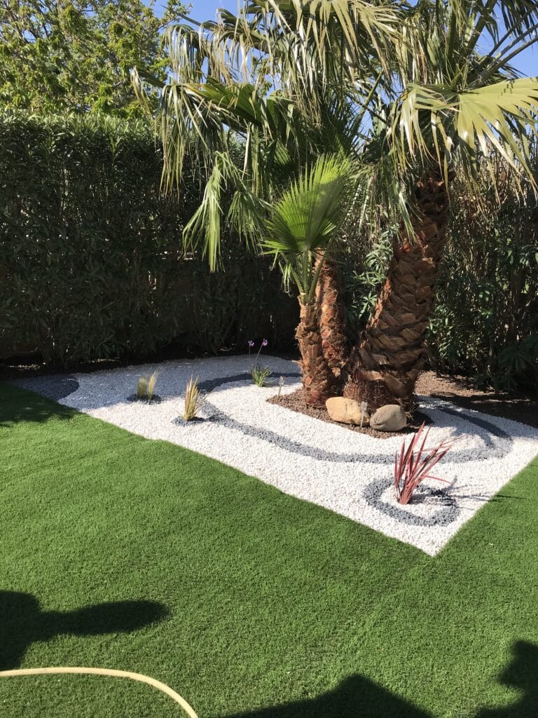 Palmier et design moderne: Gravier blanc sur gazon synthétique. Massif décoratif moderne avec palmier entouré de graviers blancs et gris à motifs sur gazon synthétique, ensoleillé.